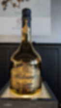 Large gold-and-black champagne bottle on display, labeled 2009 Charles de Cazanove Brut, reflecting a room.