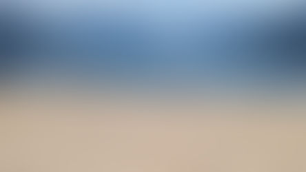 Sandy beach with people swimming and paddleboarding in a calm lake. Mountains and clouds in the background; blue tents and umbrellas dot the shore.