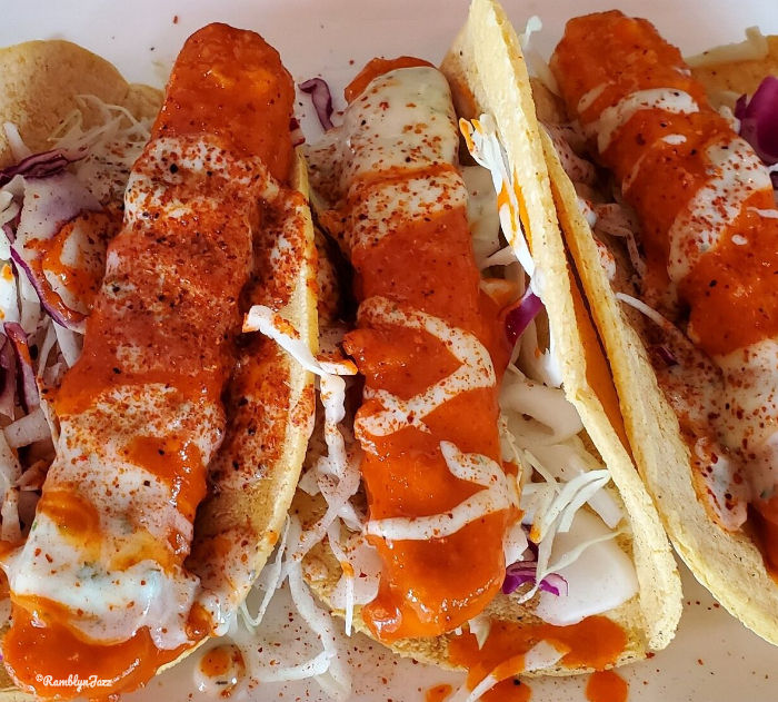 Three fish tacos with vibrant orange sauce and shredded cabbage in corn tortillas on a white plate, evoking a zesty, appetizing mood.