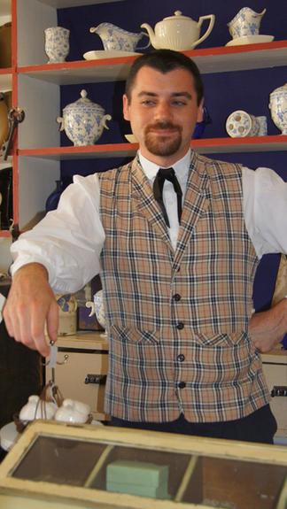 A dapper store owner in front of a display of household ceramics