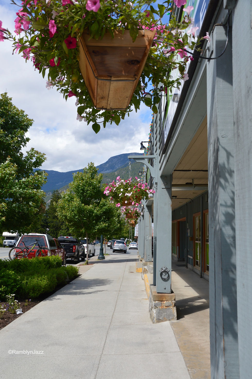sidewalk view in a small town. Hanging baskets are suspended from store fronts.