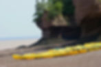 Yellow kayaks lined up on a rocky beach with rugged cliffs and sparse vegetation. Calm waters visible under a clear sky.