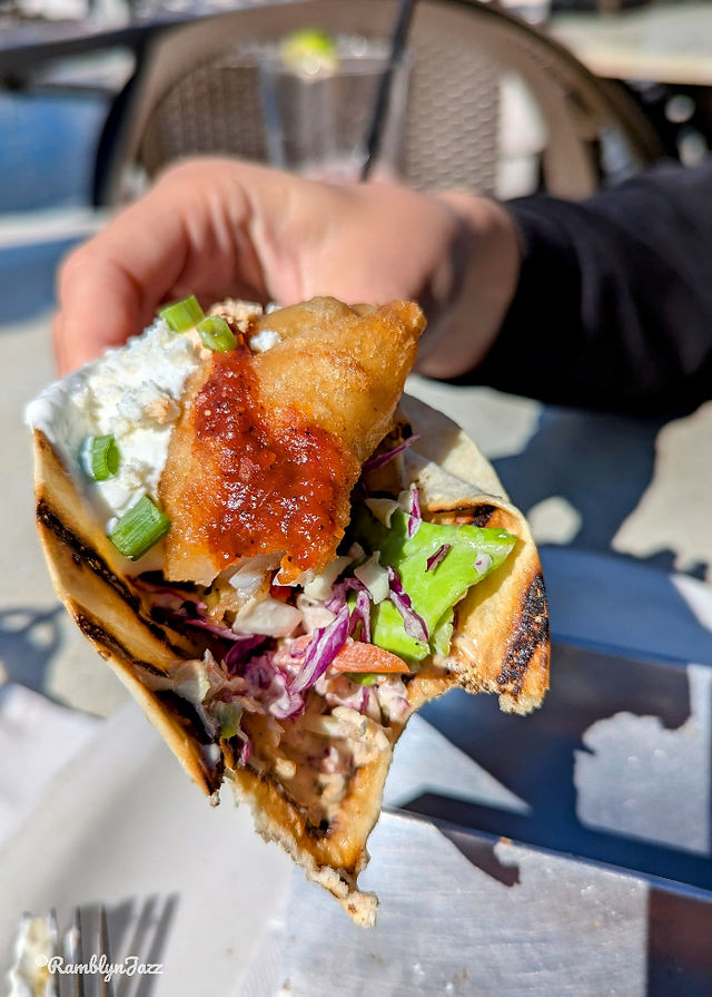 a hand holding a fish taco with a bite missing