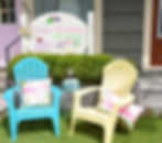 Two colorful chairs with flamingo pillows are set outside "Sugar Bubbles Bath Bakery," beside an "Open" sign, creating a cheerful vibe.