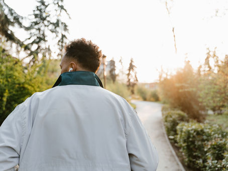 Someone walking on a path surrounded by greenery listening to a podcast about EMDR in headphones.