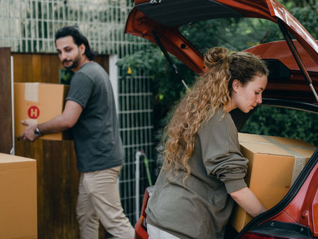 Two people loading cardboard boxes into the trunk of a car.