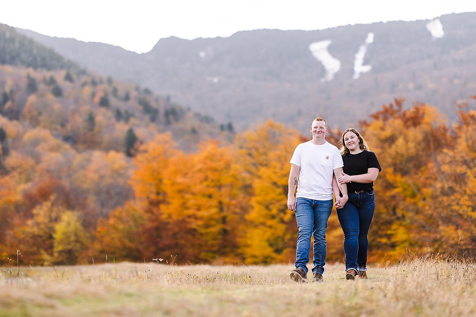 Couple walking through an autumn field during a Vermont engagement photography session.
