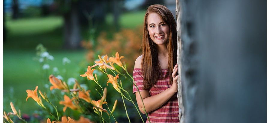 A teenage girl with long brown hair smiling next to a stone wall during her Vermont senior photo session.