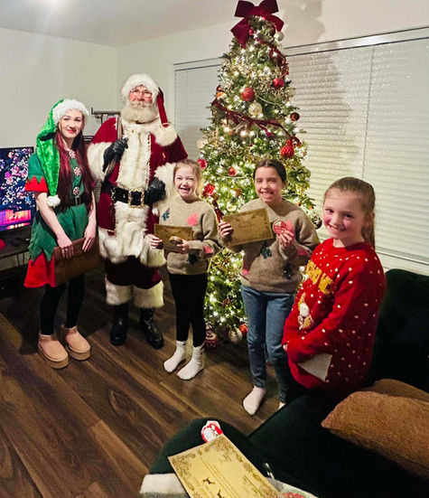 Santa, an elf, and three children by a Christmas tree