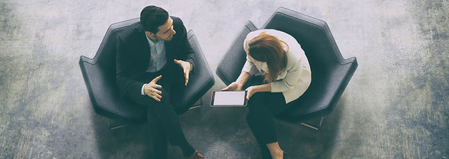 Business Meeting between a man and a woman. The woman is holding a digital tablet. The man and woman are in business attire.