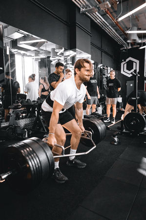 a man is lifting a barbell in a gym with others