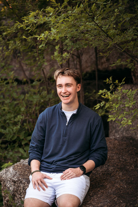 Male high school senior smiles on rocky terrain.