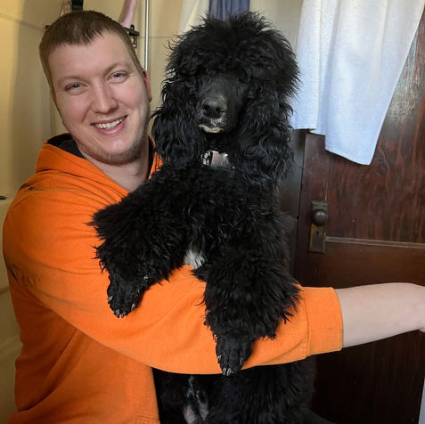 Man smiling at camera holding standard poodle in his arms