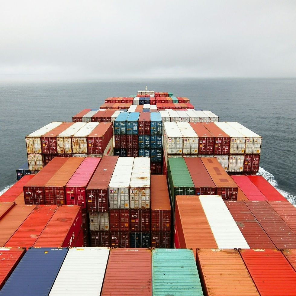 Colorful stacked shipping containers on a cargo ship at sea, with visible labels like tex, under a calm gray, hazy sky.