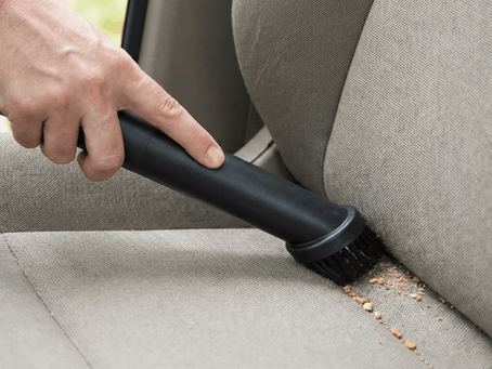 A hand using a vacuum nozzle to thoroughly clean dust and crumbs from the seams of a fabric car seat.