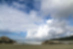 Beach scene in Tofino with large rocks, ocean waves, and an expansive cloudy sky.