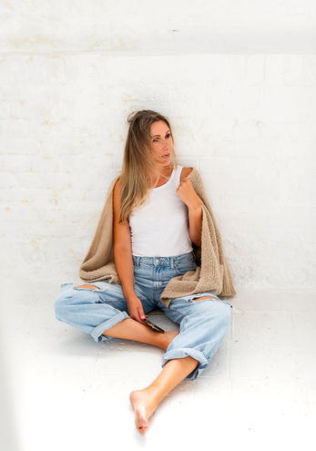 Ganzkörperportrait einer Unternehmerin sitzend an einer Wand mit Wind in den Haaren bei einem Personal Brand Shoot in Leipzig