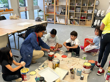 A teacher and children engage in a collaborative art project, exploring colors and creativity in a vibrant classroom environment filled with art supplies.