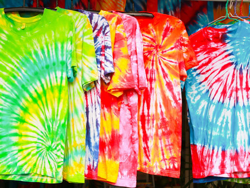 A vibrant assortment of colorful tie-dye T-shirts hangs on a display, showcasing a variety of swirling patterns and bold hues at a lively market stall.