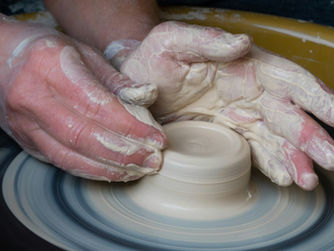 A potter skillfully shapes clay on a spinning wheel, demonstrating the art of pottery with hands covered in soft, wet clay.