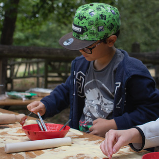 Child making a pizza outdoors, spreading sauce and cheese during a fun holiday club activity.