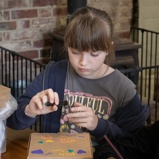 Child carefully colouring a pizza box during a creative holiday club workshop.