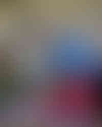 Practitioner shows off purple painty hands to a smiling child in a red apron. Messy play fun and early mark-making in full swing.