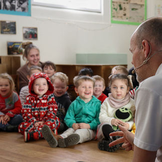 Children sit captivated during a festive performance, their faces lit with joy. A cosy classroom setting adds to the magical moment.