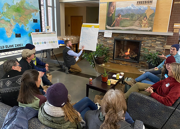 People on couches in a circle watching man write information down on poster paper.