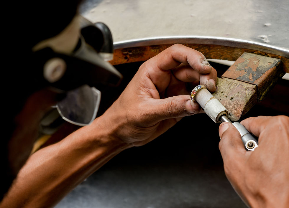 Mãos de um joalheiro da Yves Joias realizando o acabamento final em um anel com pedras naturais coloridas, evidenciando a excelência da produção artesanal própria.