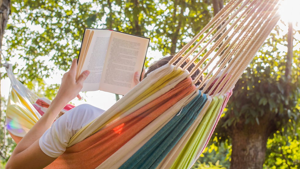 Person reading an open book while relaxing in a colorful hammock outdoors, with sunlit trees and a calm, peaceful mood.
