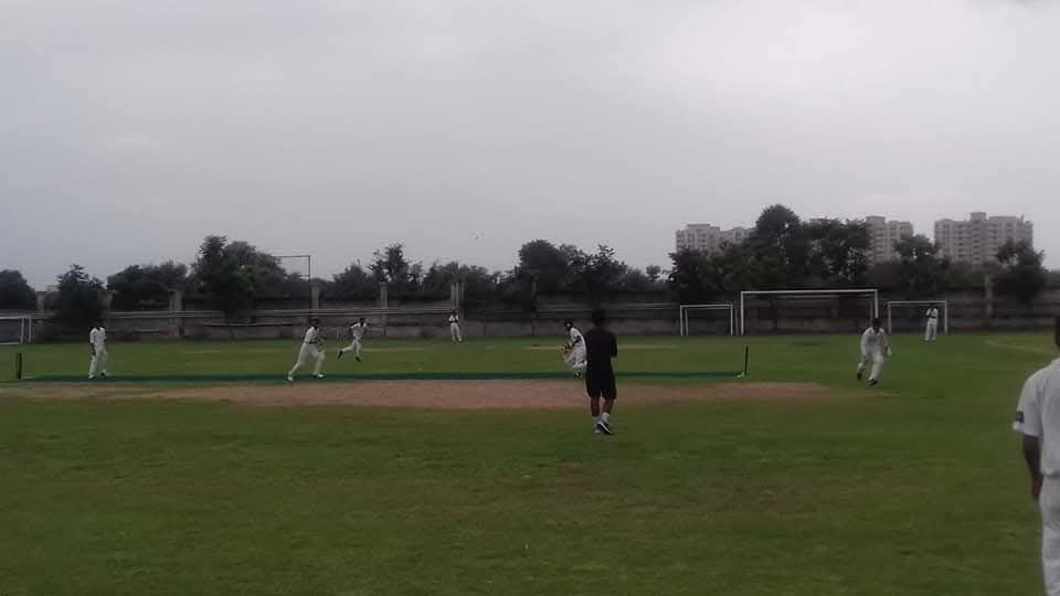 Outdoor cricket match with players on a green field under cloudy sky.