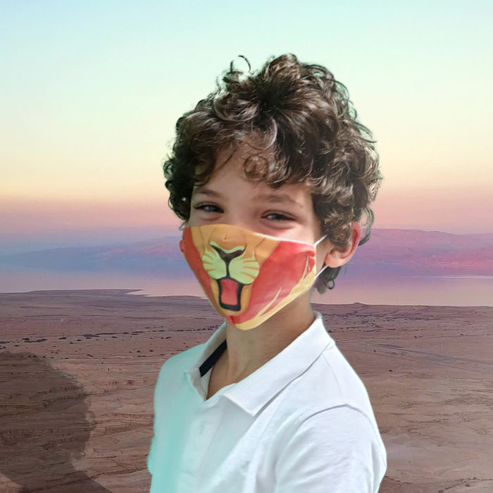 Young boy smiling outdoors while wearing a colorful cartoon-themed face mask.