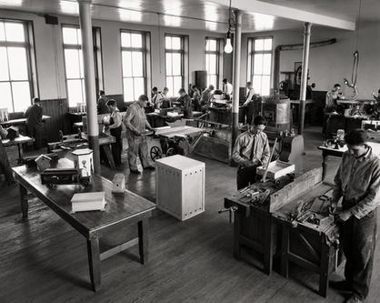 Pupils working at benches and equipment inside the SDSD Vocational Shop in the early 1900s.