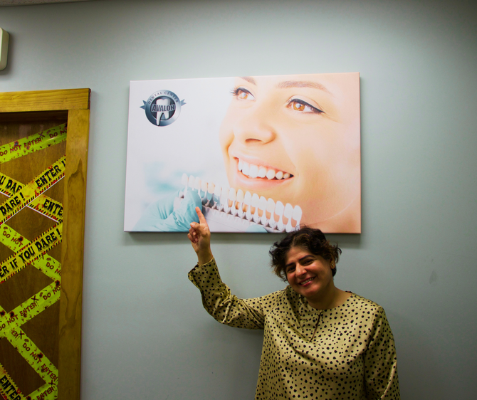 Dental professional smiling and pointing to veneer shade guide poster inside Avalon Dental Center office.