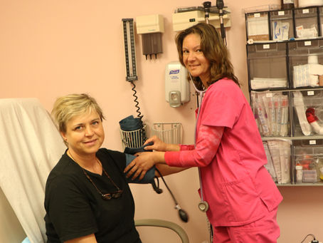 A nurse in pink scrubs takes a patient’s blood pressure during a routine check-up in a medical clinic.