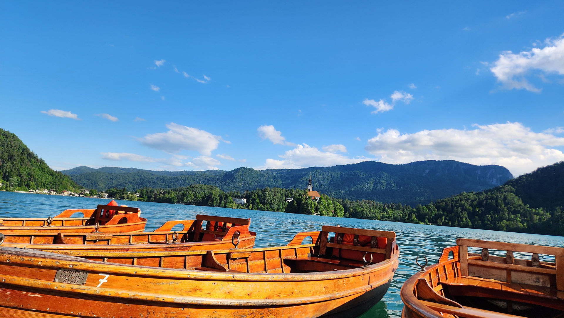 Wooden boats floating on a vibrant blue lake surrounded by lush green hills.