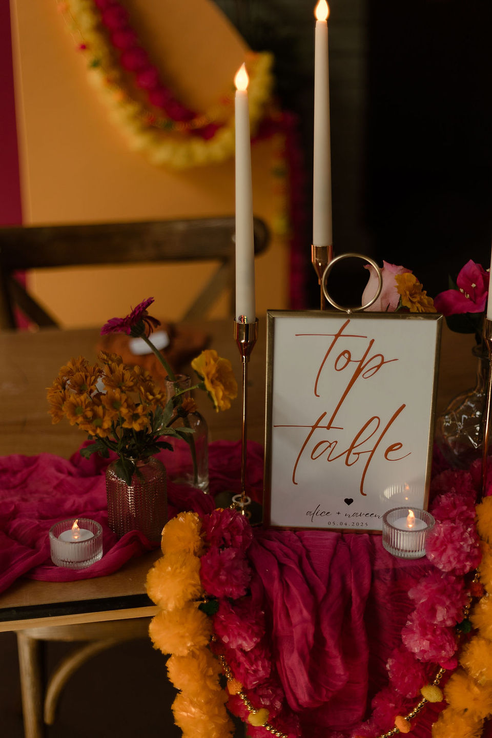 Close up of top table sign decorated with pink and yellow flowers and cloth.,