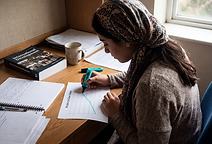 A student at a desk analysing development data, marking up a line graph headed Access to Clean Water. An international development textbook lies closed beside the chart.
