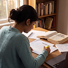 A student highlighting an organisation chart at a desk, with an open Human Resource Management textbook, handwritten notes and a laptop in a sunlit study.