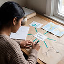A student at a desk drawing connections between different subjects around one big challenge. Hand-drawn teal lines link a central card labelled Global Challenges to a chart, a world map, a leaf, a figure and a coin.