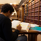 A law student seen from behind, seated at a desk in a wood-panelled university library lined with shelves of bound law reports, highlighting a passage in an open casebook. The visible page is headed Carlill v Carbolic Smoke Ball Co, with sticky-tabbed case notes and a teal notebook beside the book.