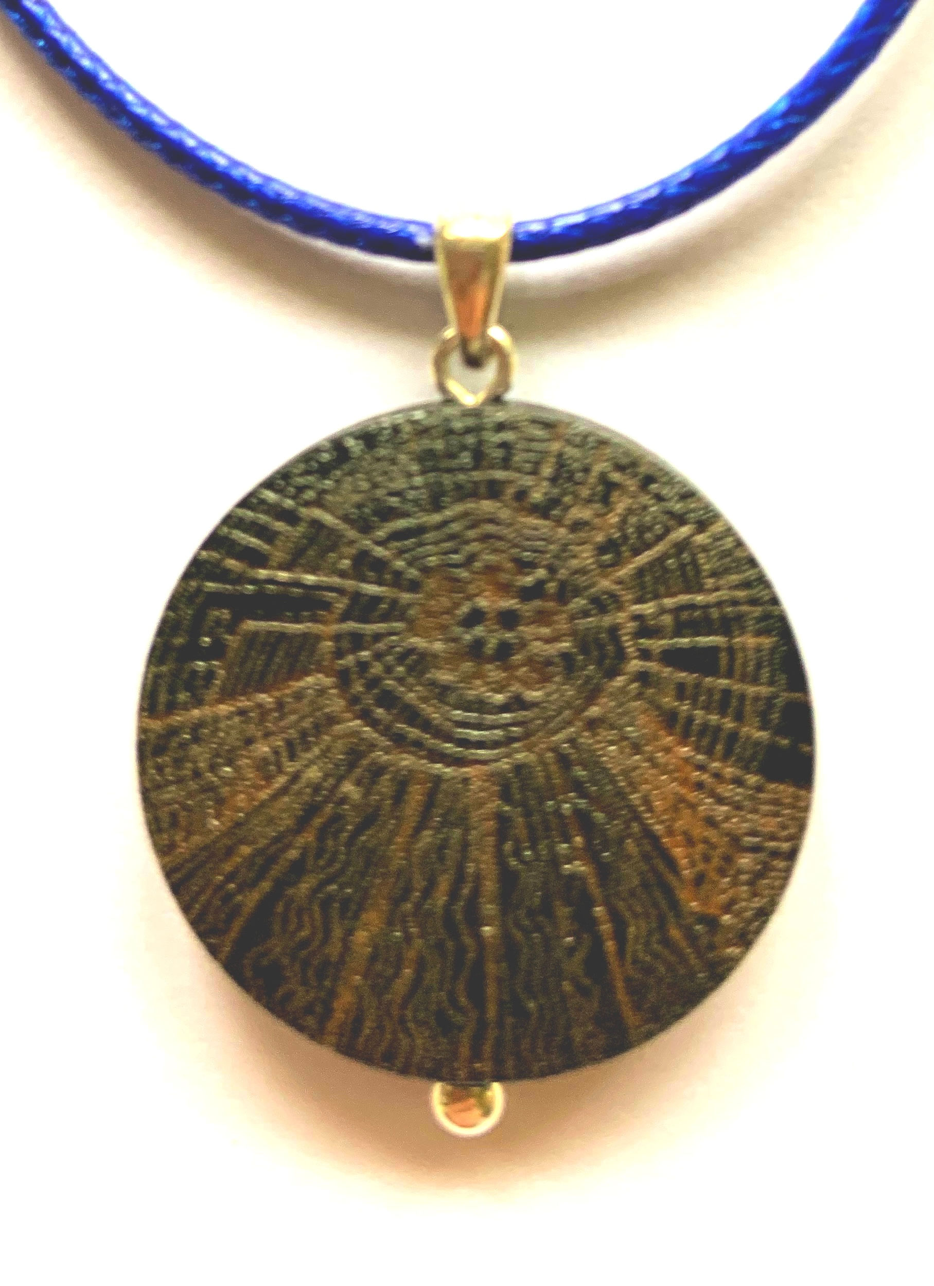 Engraved pendant with silver bail, blue cord. Circular design with radiating lines.