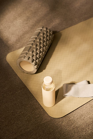 Foam roller, plastic water bottle, and elastic resistance band resting on exercise mat, fi