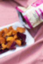 Sweet potato chips rest on a white plate next to its bag
