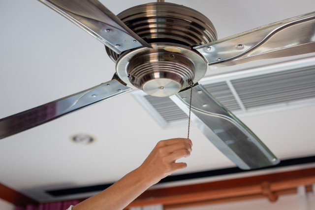 A homeowner pulls the cord on a ceiling fan to turn it on.