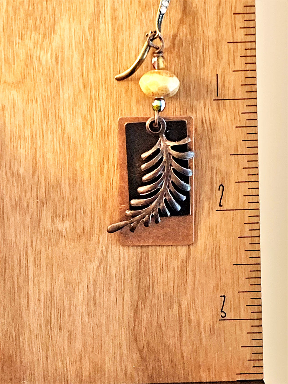 Thumbnail: Handcrafted earring with metallic fern charm on rectangular pendant, next to a ruler
