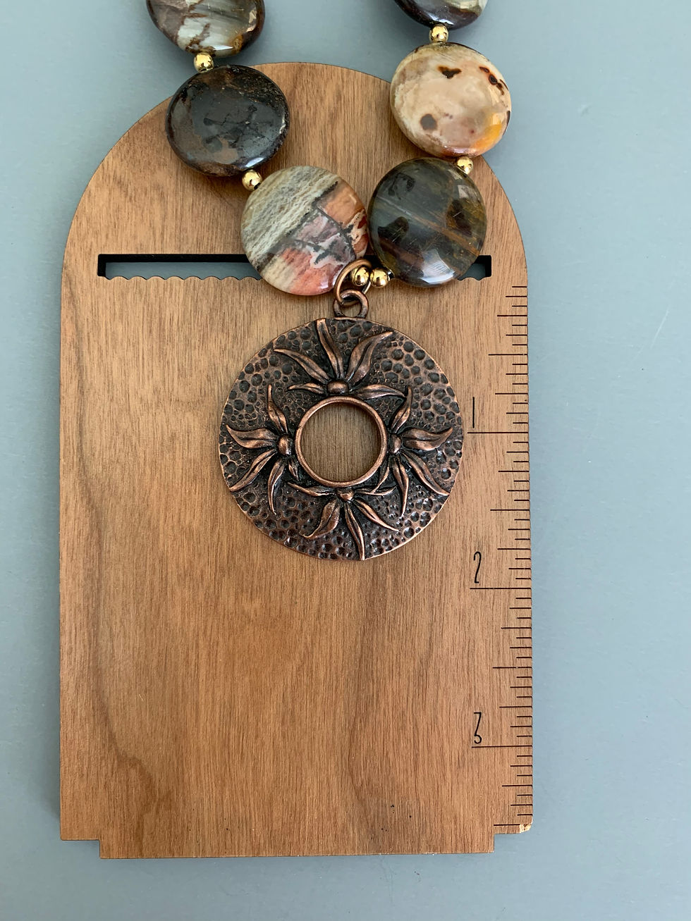 Thumbnail: Ornate copper pendant necklace with stone beads on wooden ruler