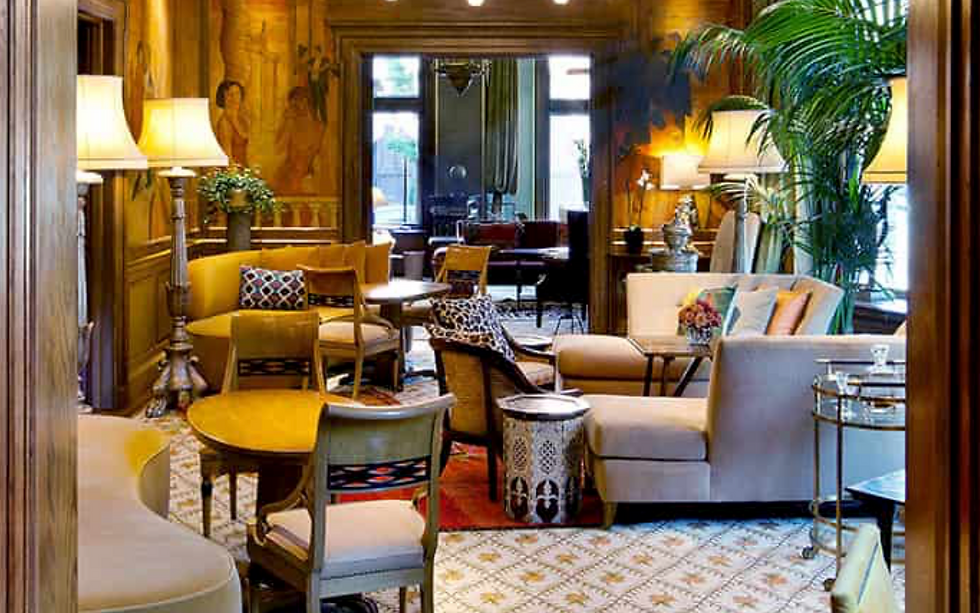 The Ivy Hotel elegant lounge with plush beige seating and patterned cushions. Warm lighting, wood panels, and green plants create a cozy, inviting atmosphere.