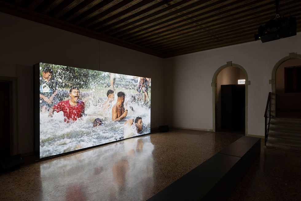 Photo of a darkened installation room with a film showing people jumping in foaming water.